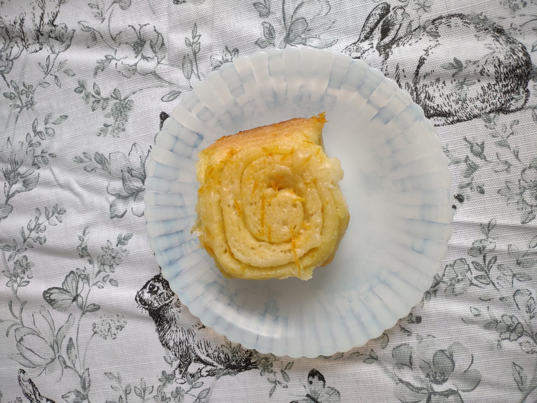 A single orange roll on a milk glass saucer on a floral tablecloth